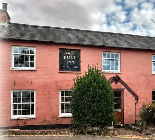 A pink-washed Suffolk cottage, once the Bull Inn, with new white flush casements and sliding sashes behind Georgian bars.