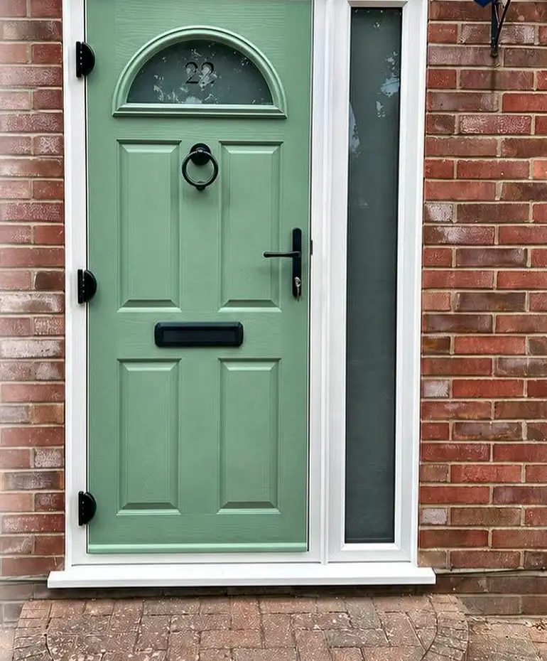 A sage green Endurance front door with half-moon glazing and a glazed side panel, set in red brick.