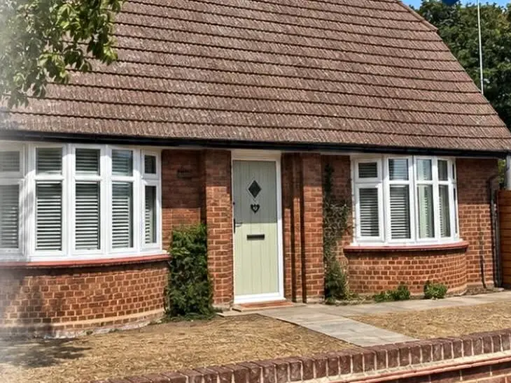 A red-brick bungalow with two new white bay windows either side of a sage green front door.