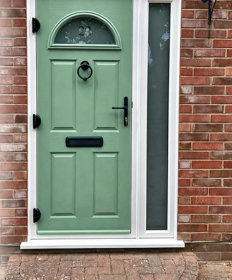 A sage green front door with half-moon glass and a glazed side panel, set in red brick.