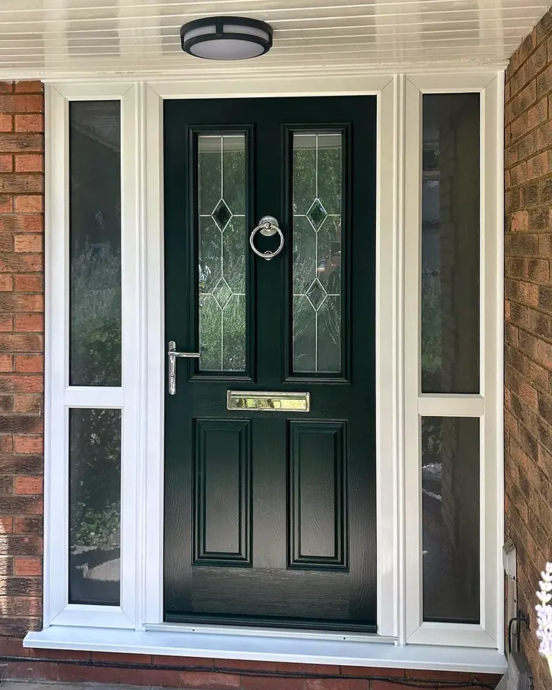 A dark green composite front door with two bevelled, leaded glass panels and a ring knocker, between glazed side panels in white frames.