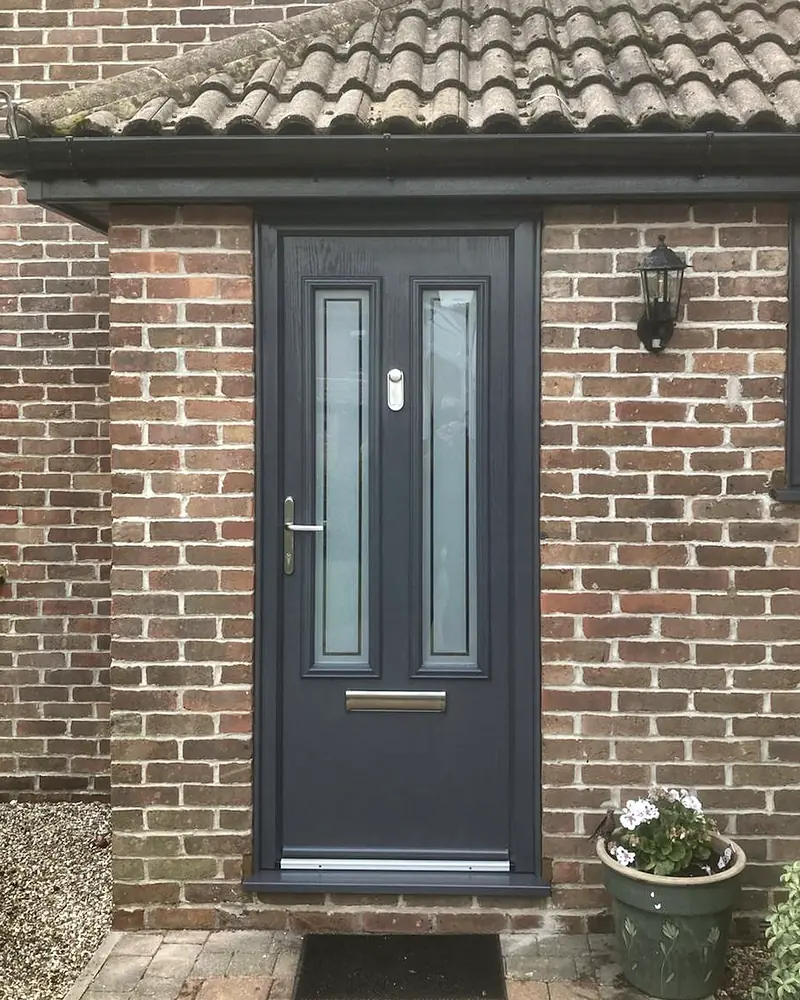 An anthracite grey composite front door with two tall glazed panels, under a tiled porch canopy in red brick.