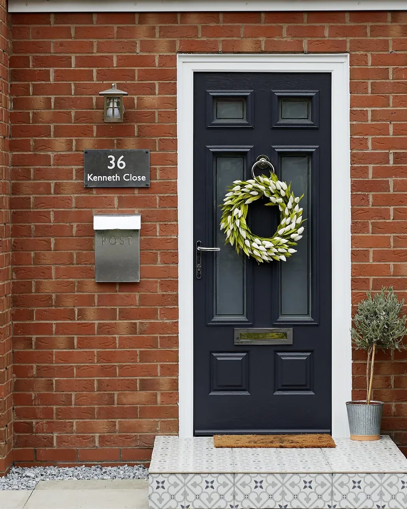 A dark panelled Endurance front door with a wreath, a brass letterplate and a house number, in red brick.