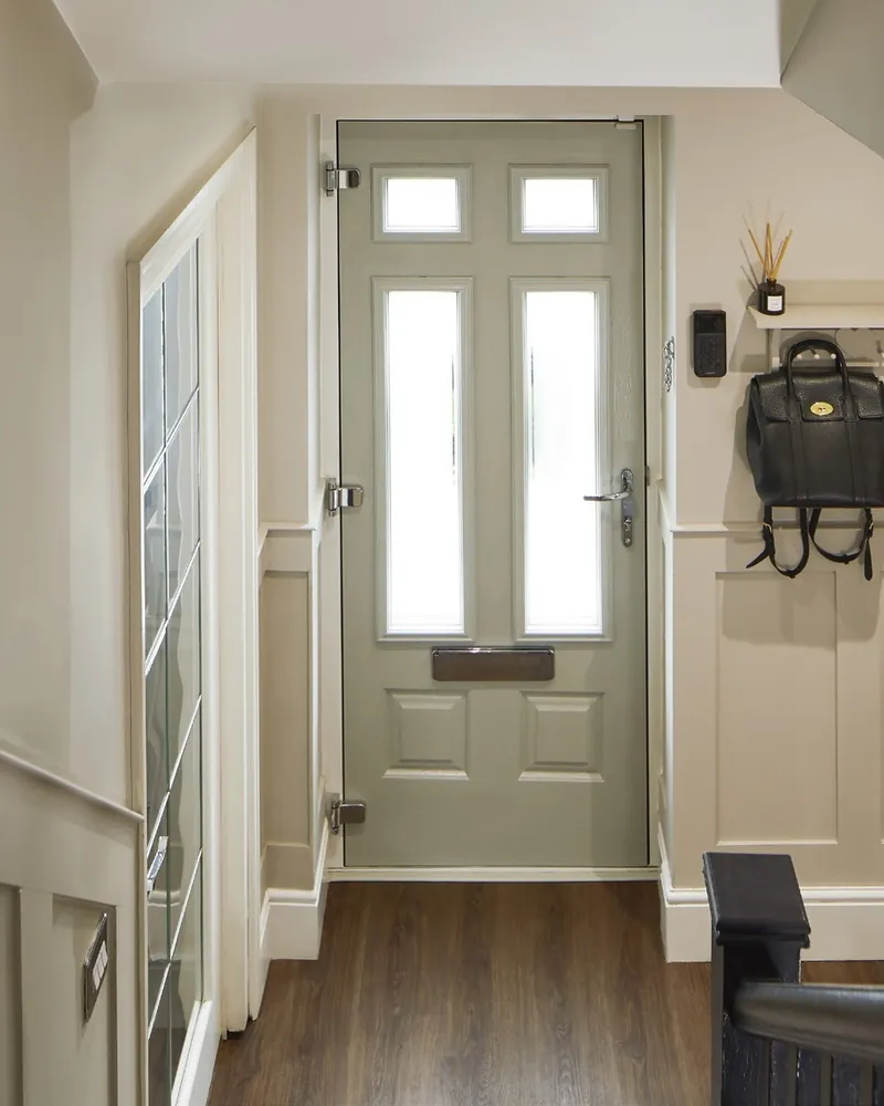 A pale sage Endurance front door seen from the hallway, with glazed panels and a bag on a hook beside it.