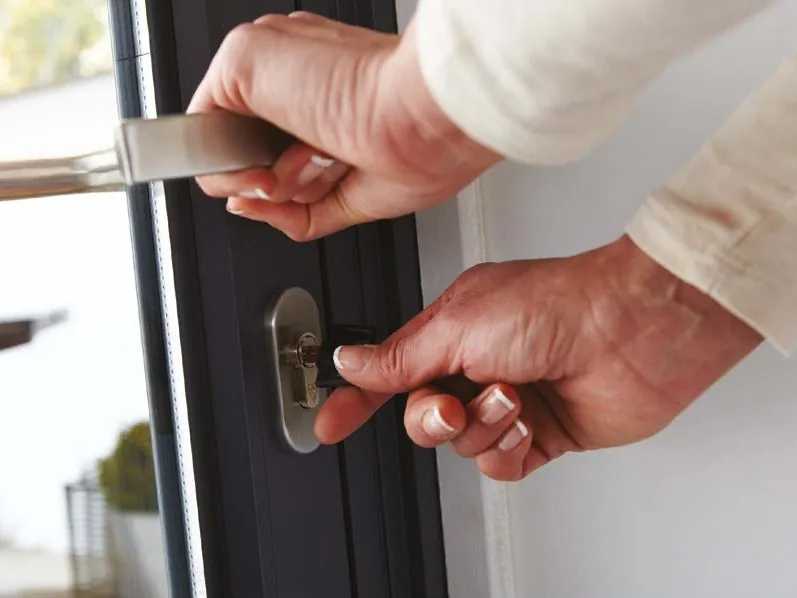 Hands turning the key in a slim dark aluminium door.