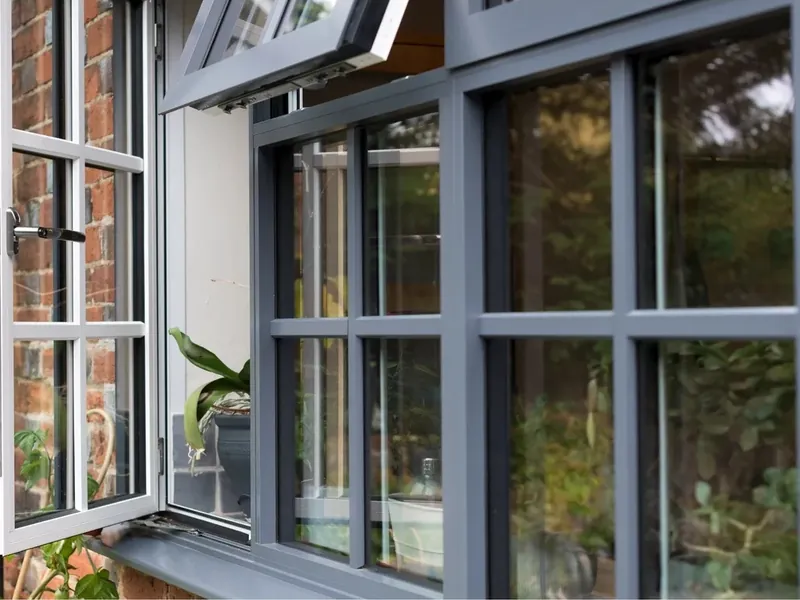 Grey aluminium casement windows with glazing bars, one sash open, in a brick wall.