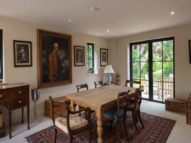 A period dining room with black steel-style French doors and windows, a dining table and portraits on the walls.