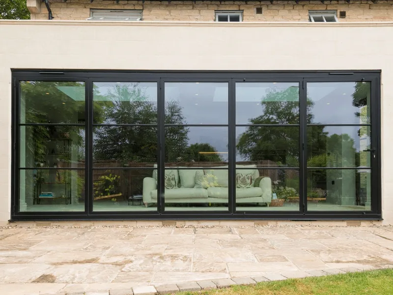 A cream rendered extension with a wall of black steel-style glazed doors, closed, with a sofa inside and a stone patio.