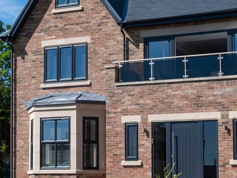 A new red-brick house with anthracite grey casement windows, a stone-trimmed bay and a matching grey front door.