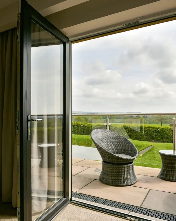 A dark-framed glazed door open onto a patio with wicker chairs and fields beyond.