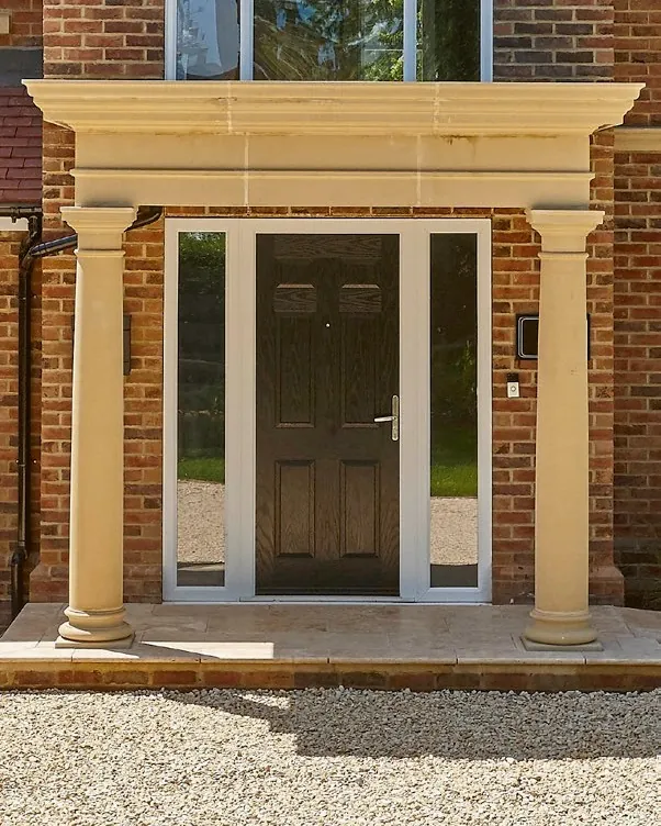 A dark front door with glazed side panels, under a stone portico with columns.