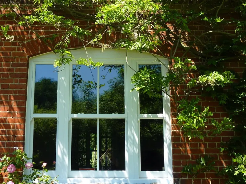 A white arched sliding sash window in a red-brick wall, framed by wisteria.