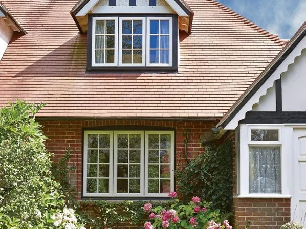 A brick and tile-hung house with a dormer, its white casement windows divided by Georgian bars, behind pink roses.
