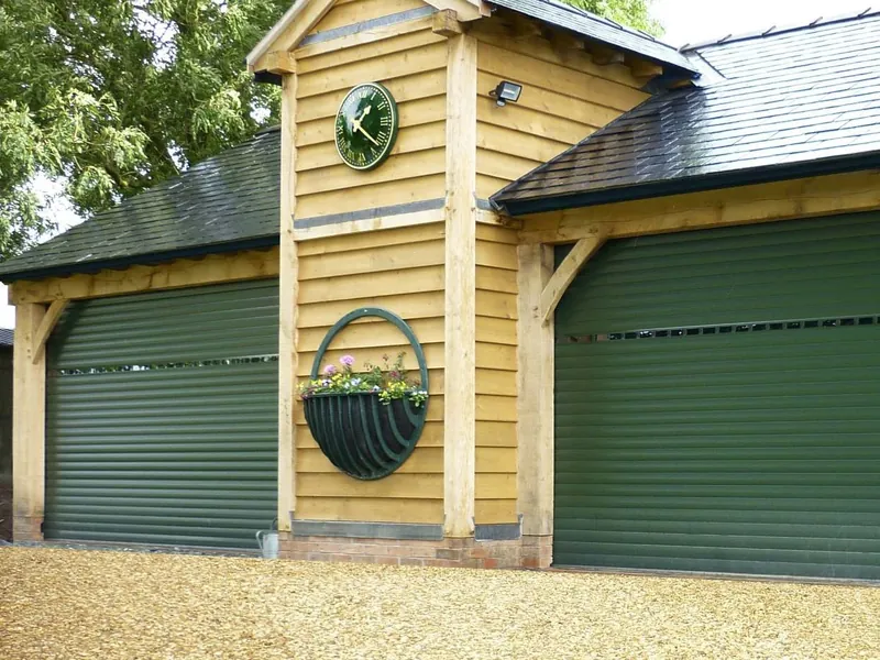 An oak-framed garage with a clock between two dark green roller doors, each with a row of vision slats near the top.