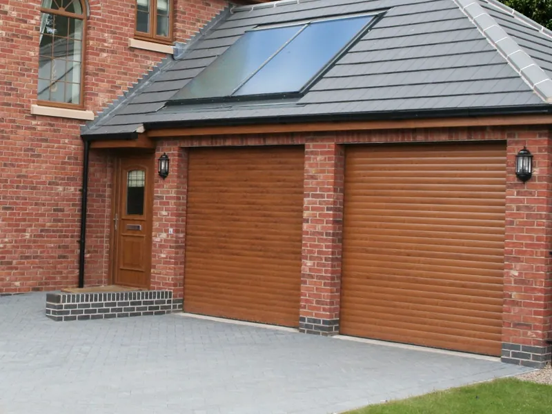 A red-brick house with two single garages side by side, each closed by a golden-oak-effect roller door.