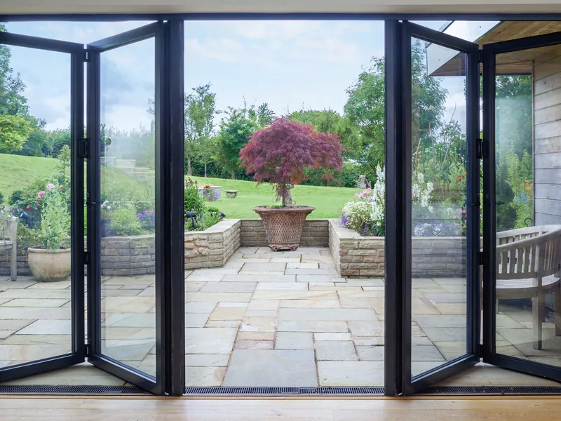 Anthracite grey aluminium bifold doors folded back at both sides, opening a room onto a stone patio and garden.