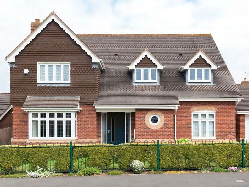 A red-brick detached house with white casement windows, a white front door and a round feature window.