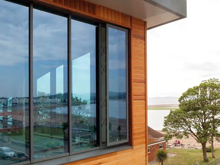 Tall dark aluminium sliding doors in a timber-clad wall, looking out over the sea.
