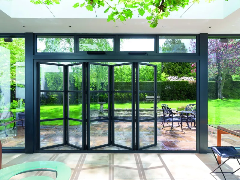 Black steel-look aluminium bifold doors with glazing bars and fanlights, folded open onto a terrace.