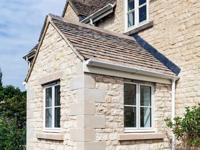 A stone cottage with slim white casement windows under a tiled roof.