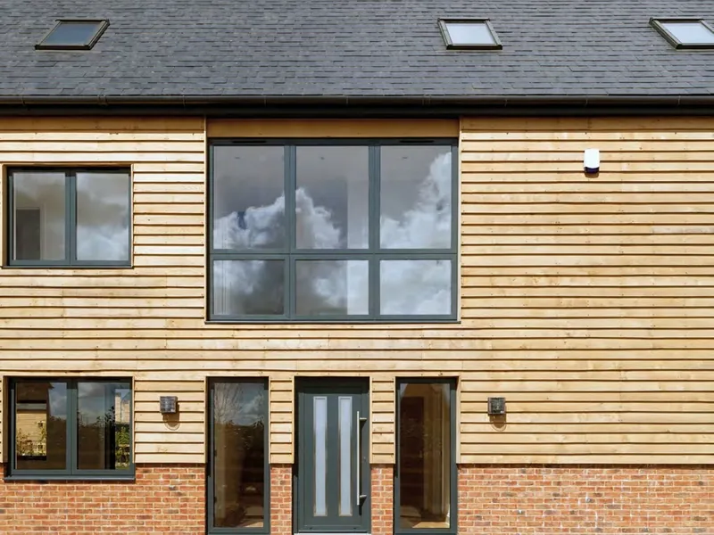 A timber-clad house with matching grey aluminium windows and a glazed grey door.