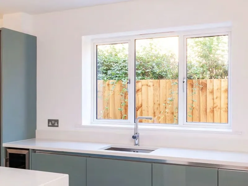 A modern kitchen with a wide white window over the sink and a garden fence beyond.