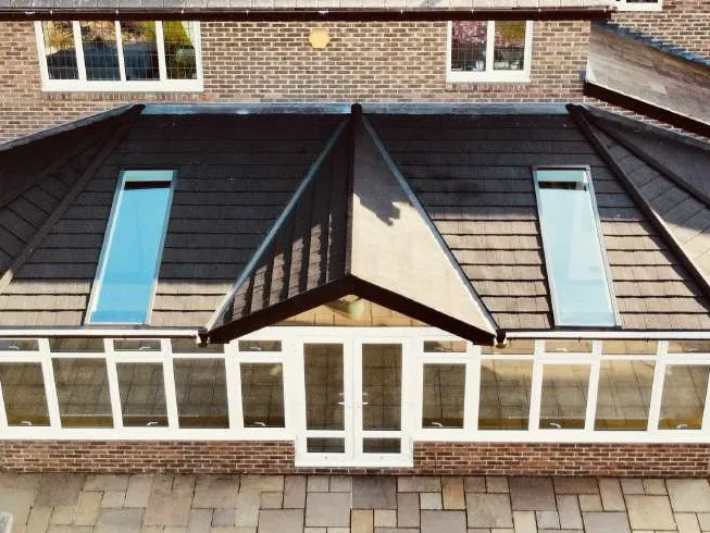 A white conservatory with a dark tiled roof, seen from above, with two long glass panels set into the tiles.