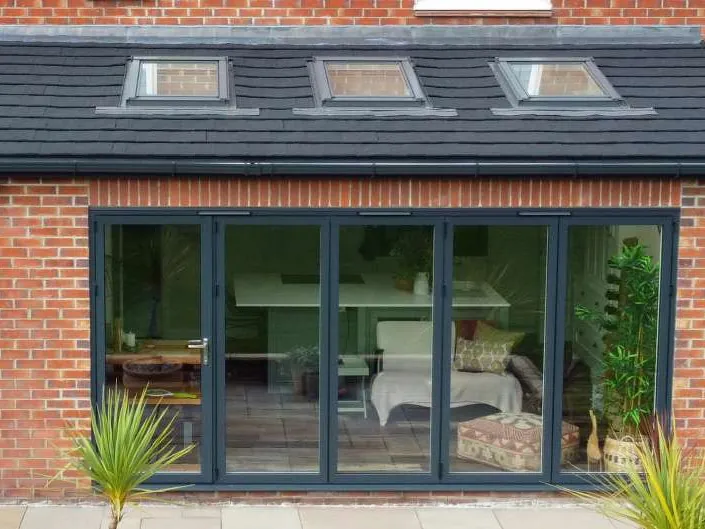 A brick extension with a dark tiled roof, three roof windows and grey bi-fold doors.