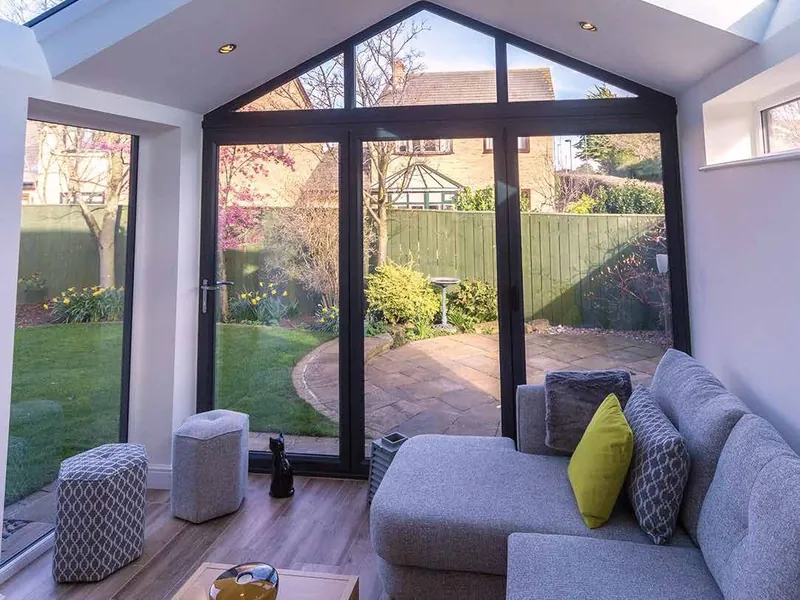 Inside a gable-fronted conservatory with a solid roof, roof windows and a grey corner sofa.