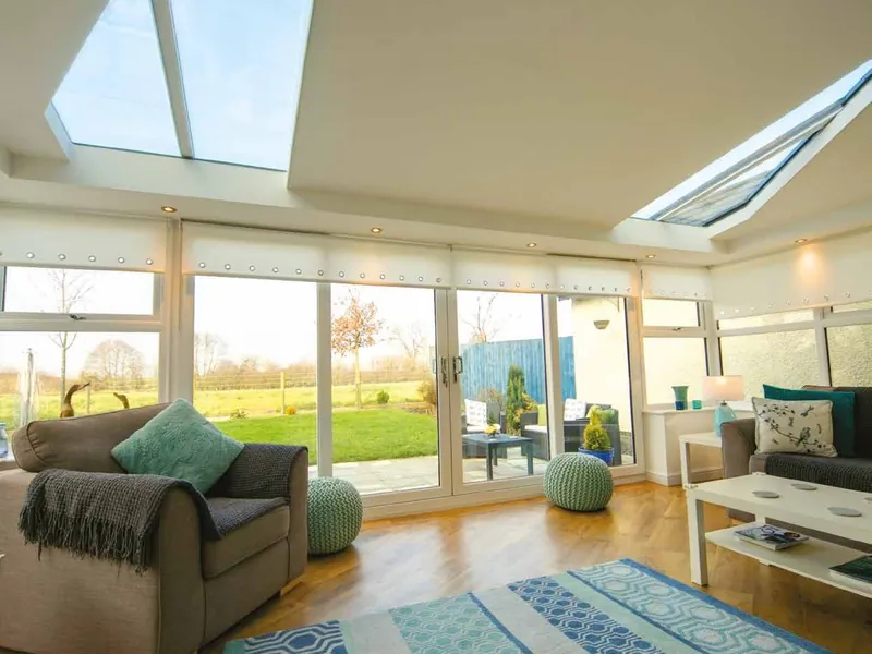 A living room under a solid roof with glazed panels and spotlights, with wide windows onto the garden.