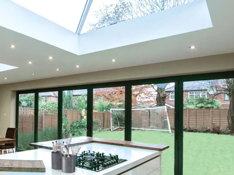 A white kitchen island with a hob under a roof lantern, with dark bifold doors open to the garden.