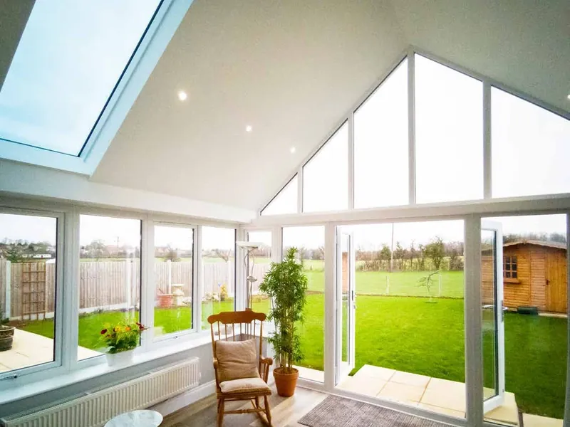 Inside a gable-end conservatory with a plastered, vaulted ceiling, long glass panels in the roof and doors open to the lawn.